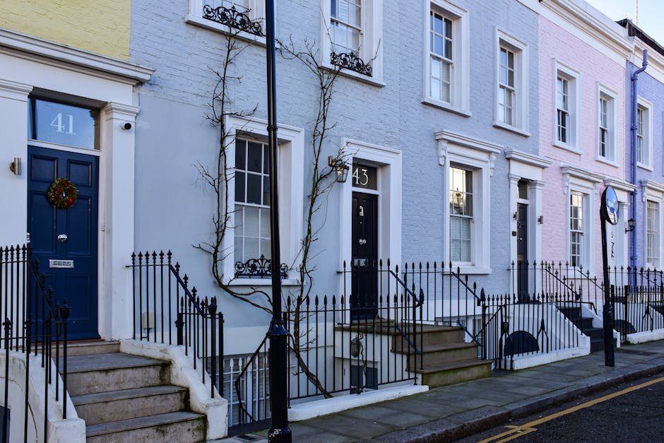 Exterior view of a row of traditional residential houses in Fulham, London, featuring brick facades with white window frames and contrasting blue doors and stair railings. The houses are built in a terraced style, with small balconies and exterior stairs leading to upper floors. The pavement in front is cobbled, and some greenery is visible in planters and small bushes near the entrances. The scene is illuminated by natural daylight, highlighting the clean and well-maintained appearance of the properties, reflecting the importance of surface cleaning and maintenance promoted by Cleaners Fulham in their domestic cleaning services.